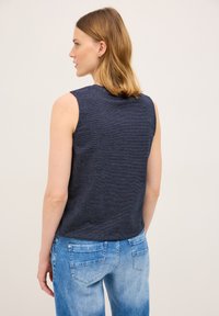 Bezrękawnik w granatowe paski wykonany z miękkiego materiału, z okrągłym dekoltem i luźnym krojem, w połączeniu z jasnoniebieskimi dżinsami.