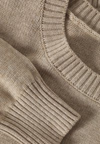 Lichtbeige gebreide trui met ribbelmanchetten en halslijn. De textuur is zacht met een losse weefpatroon door het geheel.