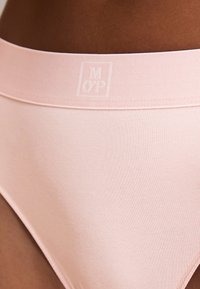 Zbliżenie na osobę noszącą jasnoróżową, bezszwową bieliznę z miękkim pasem na ciemnej skórze.