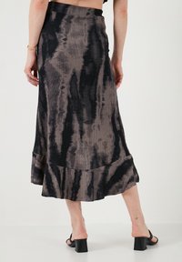 Falda maxi en un patrón de tinte anudado en negro y topo; tejido texturizado con un dobladillo acampanado. Combinada con tacos negro gruesos.