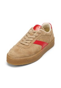 Sneaker in suede beige con dettagli in pelle rossa, lacci beige e suola in gomma testurizzata color gomma. Presenta un logo dorato sulla linguetta e sul lato.
