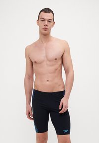 Sorte svømmebukser med sidestripe i blå geometrisk mønster, tætsiddende design, glat tekstur, længde til midten af låret og mærkelogo foran.