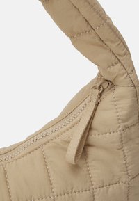 Coin de sac à main matelassé beige montrant une poignée cousue et une fermeture éclair avec une languette en tissu assorti sur un fond clair.