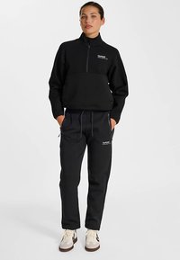 Zwart aanritsbaar sweatshirt met een contrasterend paneel, gecombineerd met zwarte joggerbroek met verstelbare trekkoord en logogegevens.