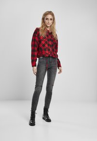 Rød og svart rutete avkortet skjorte med knapper og snøring, sammen med grå slitte skinny jeans og svarte snørebånd ankelstøvler.