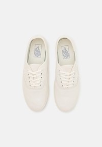 White canvas sneakers with round toe, lace-up closure, smooth texture, padded collar, and subtle logo on the insole.
