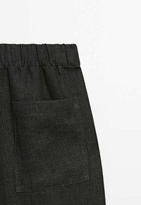 Pantalon en denim noir avec une ceinture élastique et une seule poche latérale. Le tissu présente une texture et un design décontracté.
