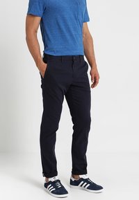 Marinblå chinos med rak passform, i bomull, med framfickor och knäppning, kombinerat med en blå T-shirt med rund halsringning och sneakers.