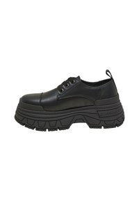 Zapatillas de plataforma negras hechas de cuero suave, con punta redondeada, seis ojales y suela de goma texturizada con un patrón de relieve distintivo.