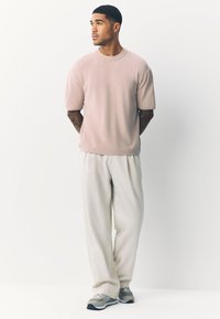 Ljusrosa kortärmad tröja med rund hals, kombinerad med löst sittande cremefärgade byxor och grå sneakers. Enkel, ren design.