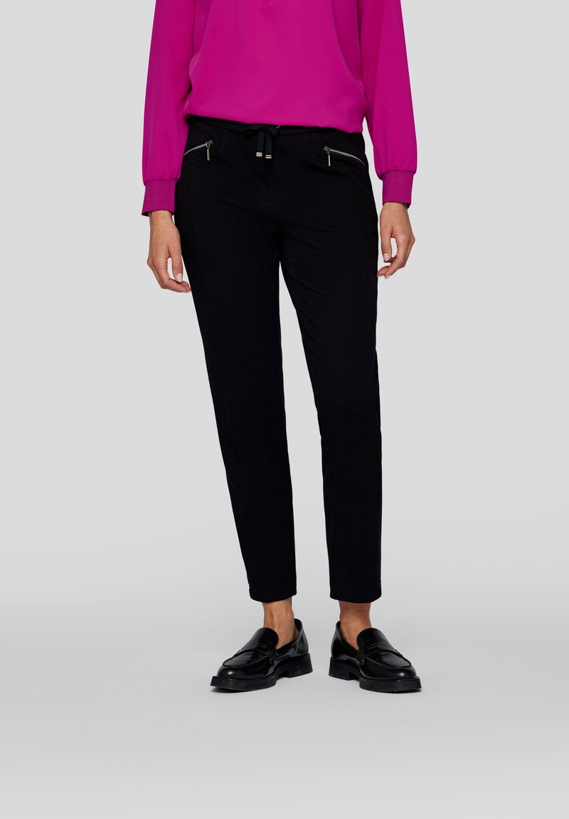 Black tapered pants with zippered pockets and drawstring waist, paired with a bright pink long-sleeve blouse and black loafers.