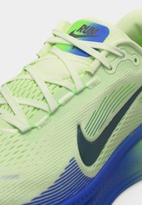 Ανοιχτό πράσινο παπούτσι για τρέξιμο Nike με μαύρο σήμα, μπλε λεπτομέρειες στην σόλα και το λογότυπο «RUN» στη γλώσσα, με λευκά δέματα δεμένα.