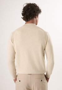Beige gebreide trui met een ronde halslijn en lange mouwen, voorzien van ribgebreide accenten op de schouders en manchetten. Soepele textuur.