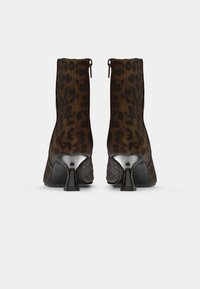 Botas de tobillo con estampado de leopardo en ante marrón y negro, con un tacón afilado y un cierre de cremallera en la parte trasera. Textura suave y forma elegante.