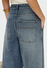 Jeans i denimbomull med en blekt blå tvätt, med hög midja, två bakfickor och synliga söm detaljer. Tyget har en något texturerad yta.