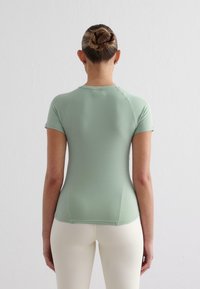 Mintgrön figurnära topp med korta ärmar, rund hals och slät textur; matchad med off-white högmidjade leggings.
