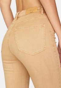 Ljust beige denimjeans med en åtsittande design, som har en sömd bakficka och en bälteetikett i tanläder. Slät textur.