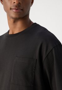 Sort bomulds t-shirt med rund halsudskæring, korte ærmer og en brystlomme med dekorative syninger. Glat tekstur.