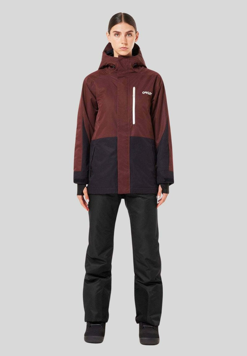 Water-resistant, two-tone jacket in maroon and black with a hood, zippered pocket, and relaxed fit, paired with black snow pants and boots.