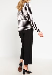 Czarno-biała, w paski, bluzka z długim rękawem w zestawieniu z czarnymi spodniami szerokimi i czarnymi butami na obcasie, pokazana z tyłu.