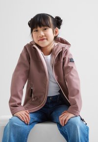 Pink hooded jacket with a smooth finish, featuring zippered pockets and a lightweight design, worn over a white shirt and blue jeans.