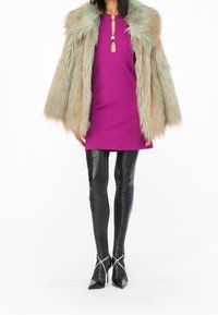 Faux fur-kappa i grönbrun, lila klänning med nyckelhålsdetalj, glänsande svarta leggings och spetsiga svarta klackar med korsade remmar.