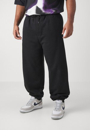Black sweatpants with a drawstring waistband, elastic cuffs, and a relaxed fit, paired with gray and white sneakers featuring navy accents.