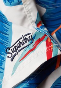 Bañador con un vibrante patrón azul y blanco con acentos en rojo y naranja. Logo bordado de "Superdry" en navy sobre la tela.