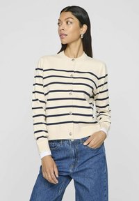 Bēža kardigāns ar tumši zilām svītrām, ar apaļu apkakli, pērļu izskata pogām un garām piedurknēm. Saskaņots ar augsto vidukli džinsiem.