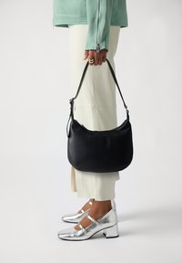 Borsa a tracolla in pelle nera con forma curva, chiusura a zip e tracolla regolabile. Texture liscia con dettagli di branding minimi.