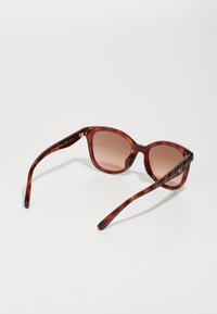 Ochelari de soare cu ramă în tip tortoise, ușor în formă de ochi de pisică, lentile de culoare maronie cu un gradient, și brațe subțiri cu accente aurii discrete.