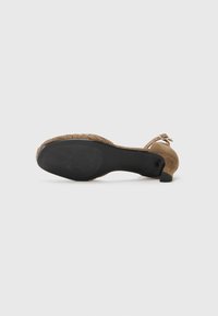 Sandale à talon haut en daim marron, avec une semelle texturée, une sangle réglable, un dos ouvert et un talon effilé. Semelle extérieure noire lisse.
