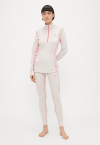 Μπλούζα με μακριά μανίκια και φερμουάρ, και εφαρμοστά κολάν σε ανοιχτό ροζ με σκούρες ροζ λεπτομέρειες. Το ύφασμα έχει ένα διακριτικό μοτίβο και λεία υφή.