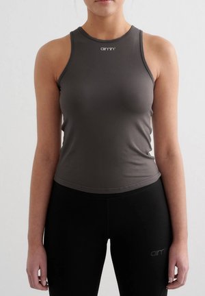 Donna che indossa un top sportivo senza maniche grigio scuro e leggings neri, in piedi davanti a uno sfondo chiaro e uniforme.