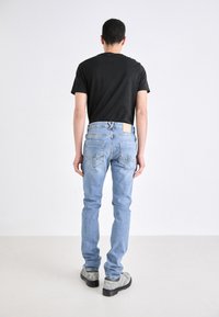 Světlé modré džínové kalhoty slim fit, pět kapes, viditelné švy a obdélníková nášivka na zadním pásku. V kombinaci s černým tričkem.