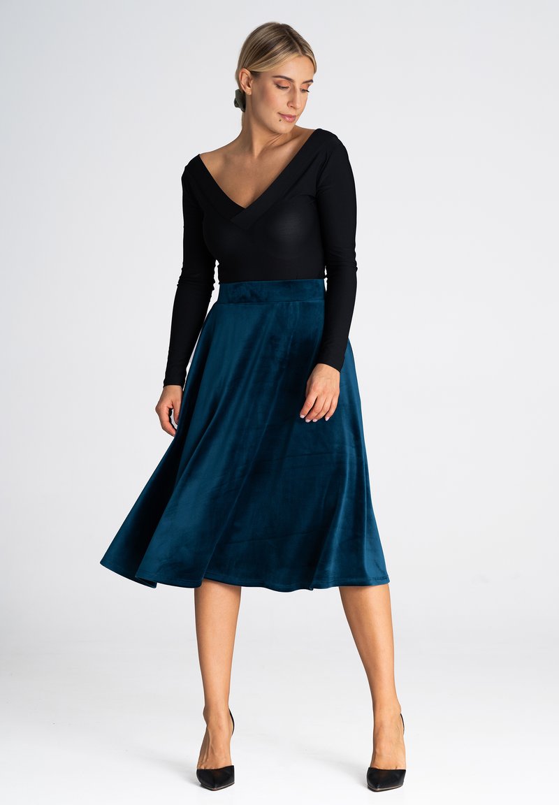 Czarny bodysuit z długim rękawem i dekoltem w kształcie litery V, połączony z turkusową, plisowaną spódnicą do kolan, wykonaną z miękkiego, gładkiego materiału. Całość dopełniają czarne szpilki.