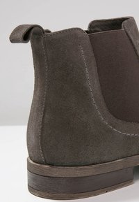 Botín Chelsea de ante marrón con panel lateral elástico, tirador en la parte trasera y tacón de madera apilada.