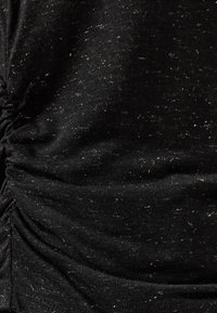 Primo piano di un tessuto nero con fini punti bianchi e una texture arricciata lungo il lato sinistro.