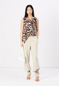 Top senza maniche marrone e bianco a fantasia abbinato a pantaloni beige a gamba larga. Accessoriato con una borsa bianca e sandali color sabbia.