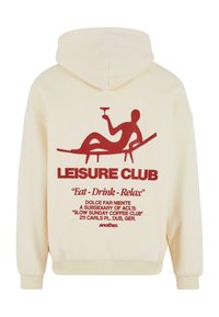 Felpa crema con stampa grafica rossa che riporta il testo "LEISURE CLUB," una figura rilassata e ulteriore testo. Tessuto morbido e polsini aderenti.