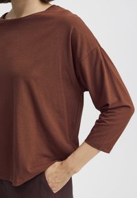 Top in cotone morbido di colore marrone, con una vestibilità comoda, scollo a girocollo ampio e maniche a tre quarti, caratterizzato da sottili spacchi laterali all'orlo.