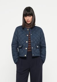 Marine quilted jakke med rund krage, gull-knapper og frontlommer. Har et cropped design, kombinert med en brun stripet genser.