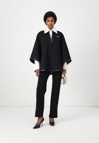 Juodas panka su aukštu apykakle, su užtrauktuku ir odinėmis detalėmis, dėvima ant baltos marškinėlių ir juodų kelnių, derinama su juodais aukštakulniais.