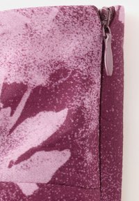 Close-up af en lilla stofpose med et blomsterprint og en matchende lilla lynlås på højre side.