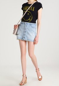 Svart t-shirt med gul grafik, ljusblå denimkjol med knappar fram, fransad nederkant och beige blockklacksandaler.