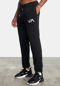 Zwarte sweatpants met een trekkoord in de taille, zijzakken en een grijs logo. De stof is zacht met een gladde textuur en aansluitend bij de enkels.