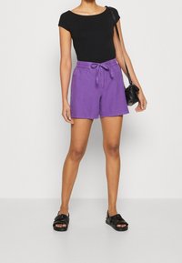 Lila bomullsshorts med elastisk midjeband och dragsko. Parat med en svart tajt topp och svarta sandaler med öppen tå. Enkelt mönster.