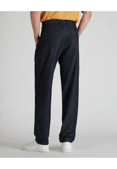 Pantaloni in denim scuro con taglio dritto, dotati di tasche laterali e risvolti, abbinati a sneakers bianche.