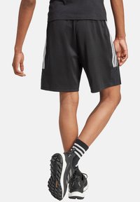 Schwarze Sportshorts mit kontrastierenden weißen Seitenstreifen, die eine glatte Textur und einen lockeren Schnitt aufweisen. Zusätzlich sind schwarze Laufschuhe mit Profil abgebildet.