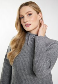 Pulover gri cu model rib, cu guler înalt și detalii cu șnur. Textură moale, mâneci lungi și design ajustat.